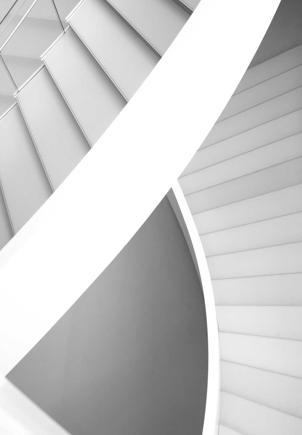Schwarzweißfotografie einer modernen Wendeltreppe mit weißen Stufen und einem geschwungenen weißen Geländer